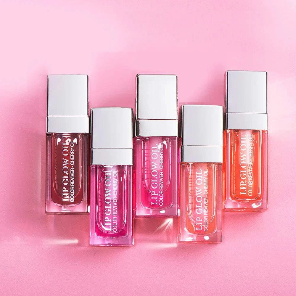 Assorted bottles of moisturizing lip balm gloss in various pink shades on a pink background.